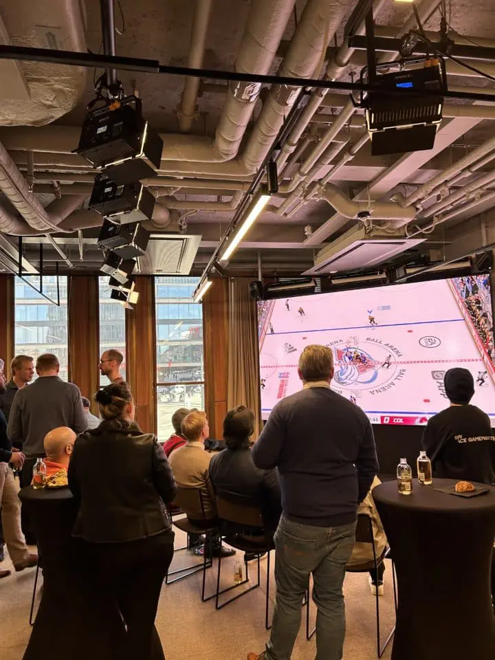 People watching hockey on a big screen in a conference room. Människor ser hockey på storbildsskärm i ett konferensrum.