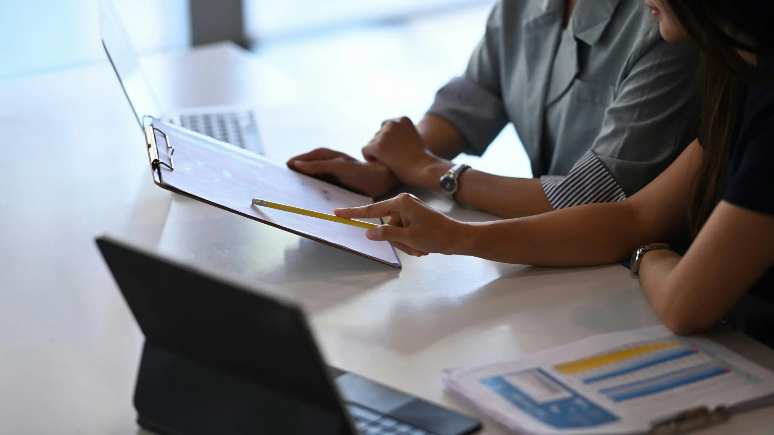 Two people are discussing a document. One of them is pointing with a yellow pencil.
