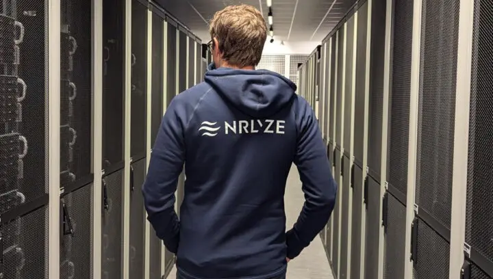 Person wearing a hoodie with the Nrlyze logo on the back walks into Bineros' server room.