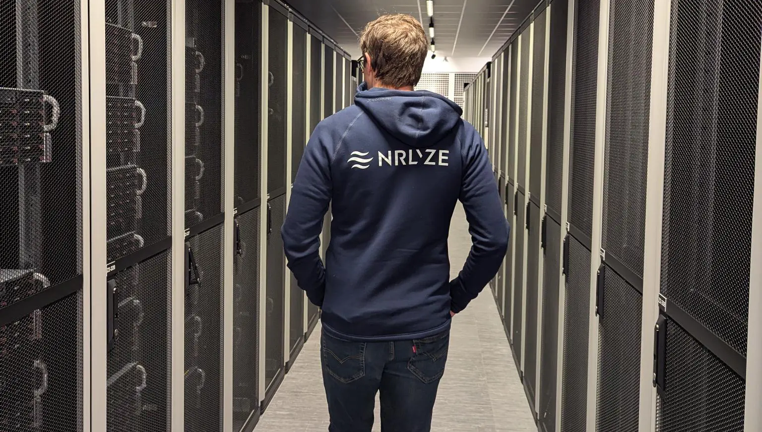 Person wearing a hoodie with the Nrlyze logo on the back walks into Bineros' server room.