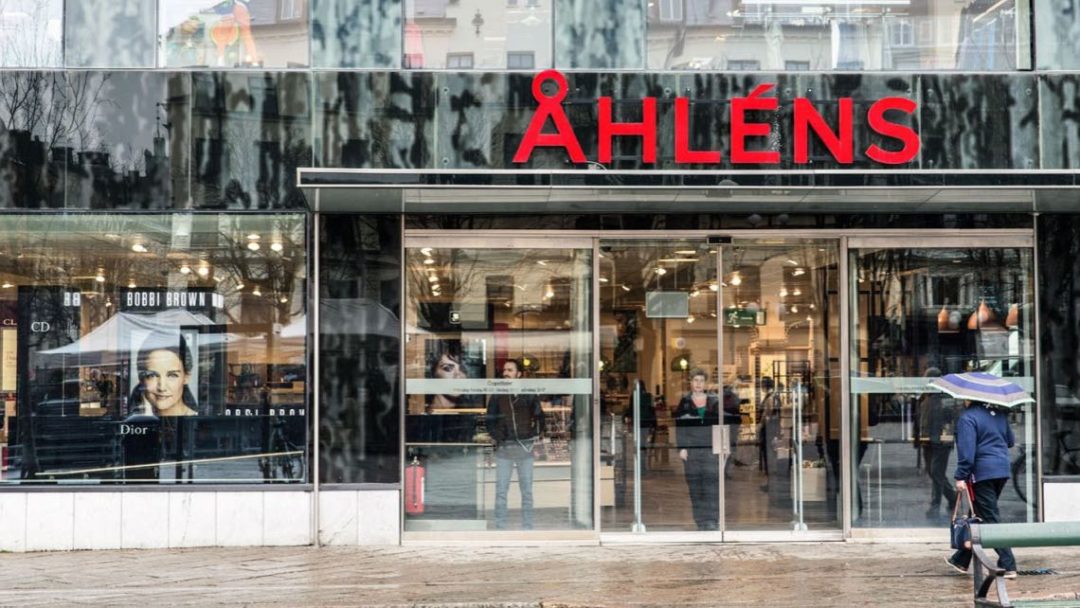 Inngangen til Åhléns butikk, med store glassvinduer og folk som går forbi med paraply.
