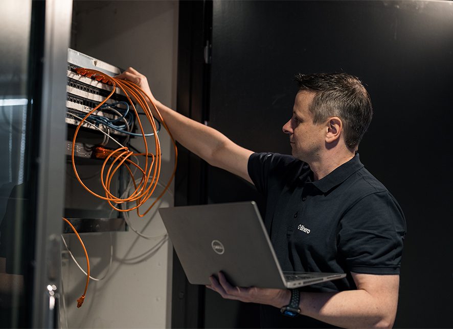 An IT technician at work holding a laptop and connecting orange cables