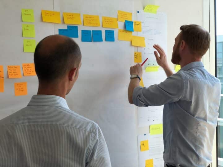 Two colleagues plan using post-it notes on a wall.