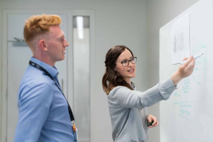 Girl explaining something on a whiteboard to a boy. Tjej förklarar något på en whiteboard för en kille.