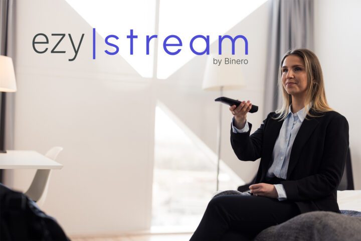 EzyStream logo. A hotel guest sits on the bed and points a remote control at a television.