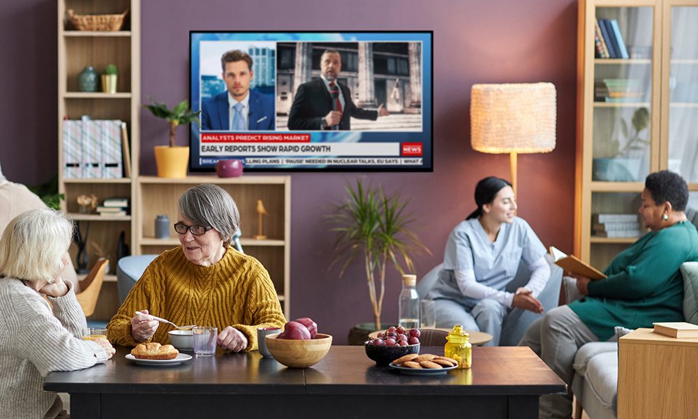 Elderly people in a retirement home with a TV on the wall showing news. Äldre människor på ett äldreboende med en TV på väggen som visar nyheter.