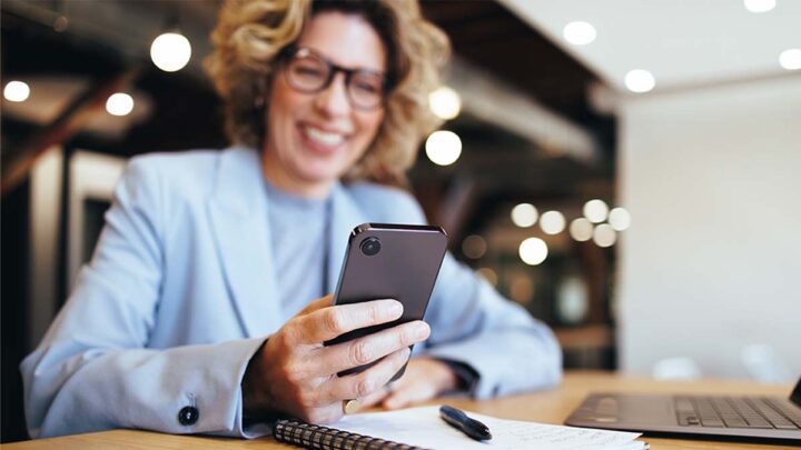 Smiling businesswoman looking at her smartphone in an office. Leende affärskvinna tittar på sin smartphone på ett kontor.