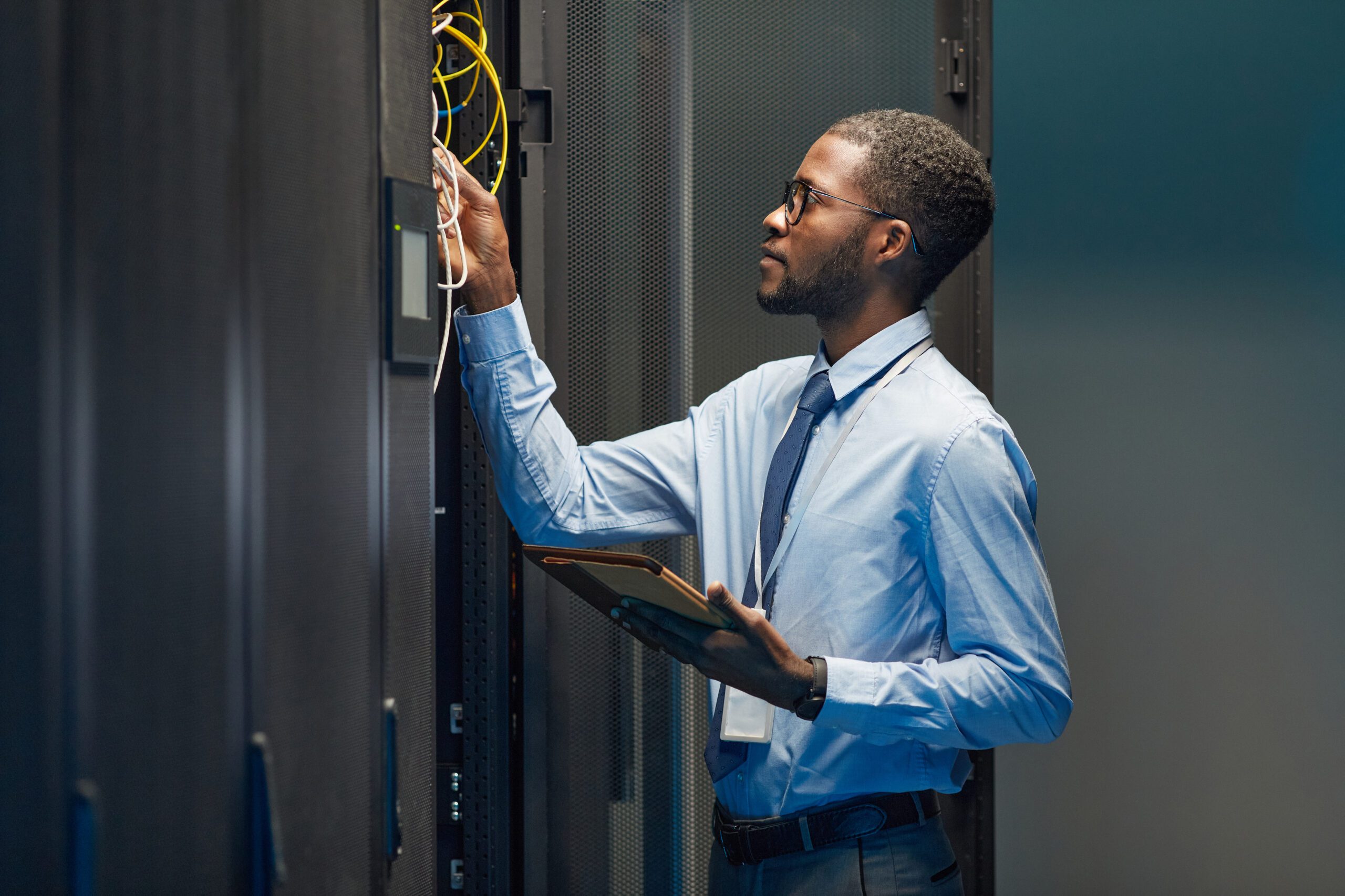 An IT technician works on connecting cables while holding a tablet.