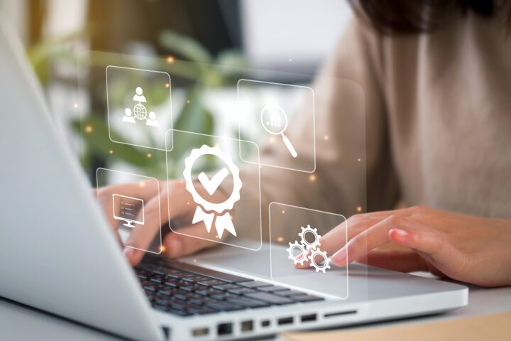En person, der arbejder på en bærbar computer. Illustrationer af tandhjul, en computer, en prisseddel og et forstørrelsesglas.