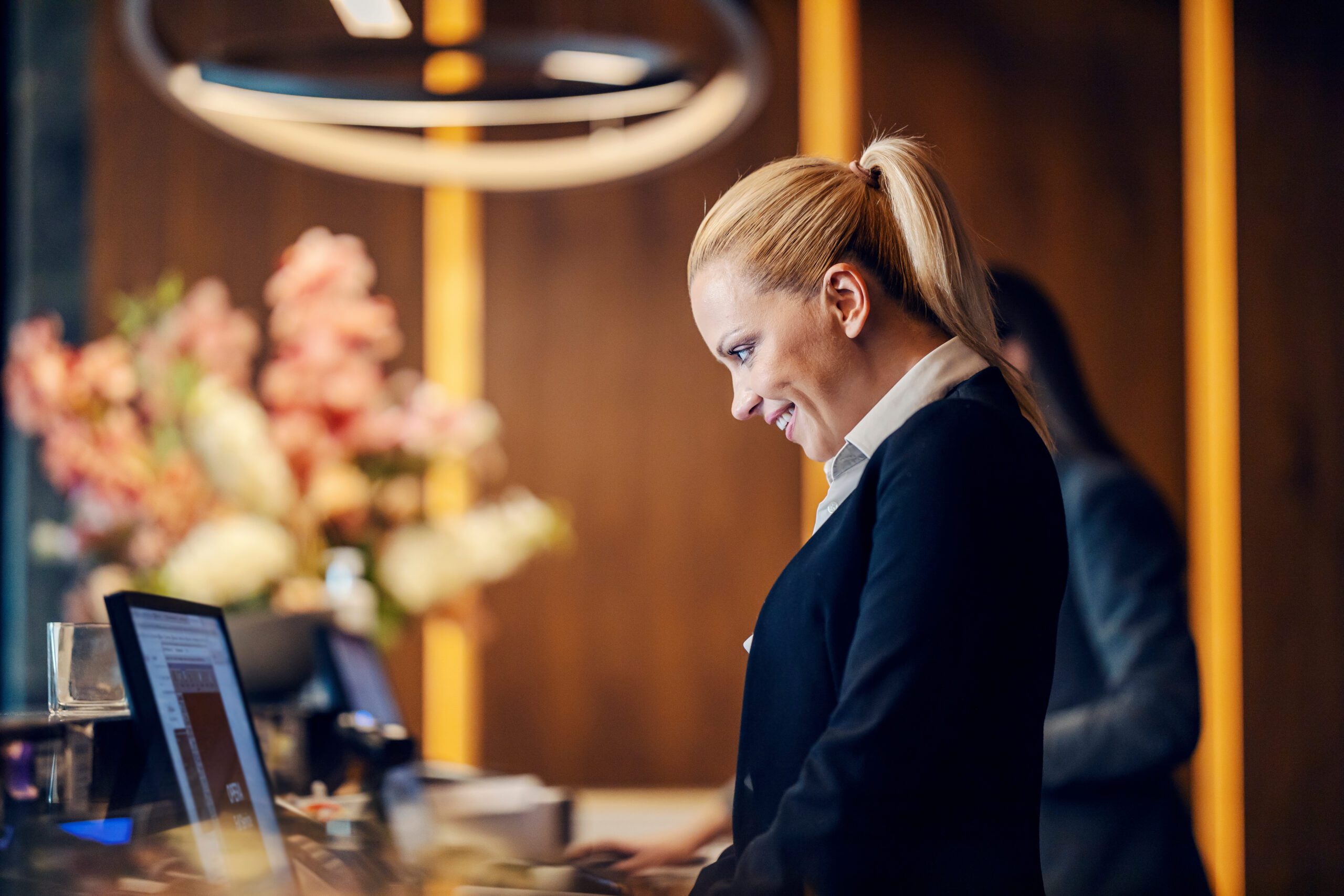 A happy receptionist is making an online reservation on computer while standing at reception.