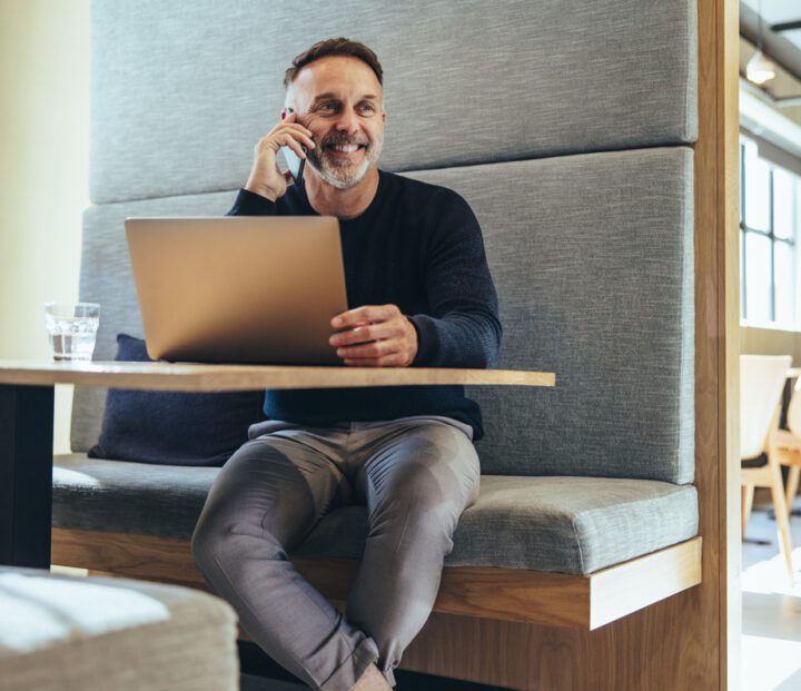 A person sits apart, chatting happily on the phone with a laptop in front of them.