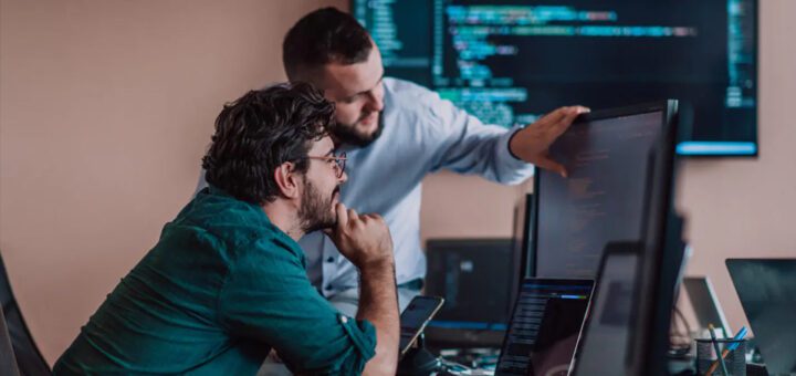 Two people working with code on multiple computer screens