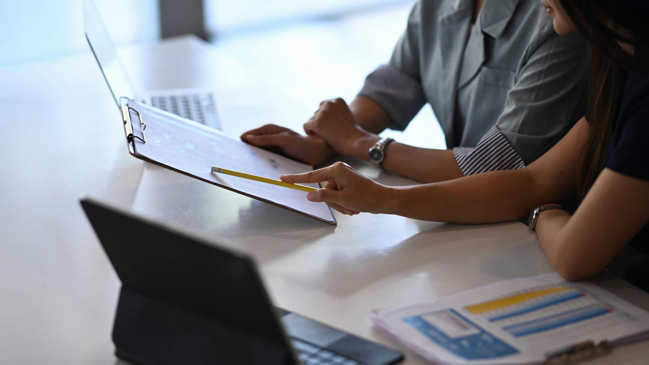 Two people are discussing a document. One of them is pointing with a yellow pencil.