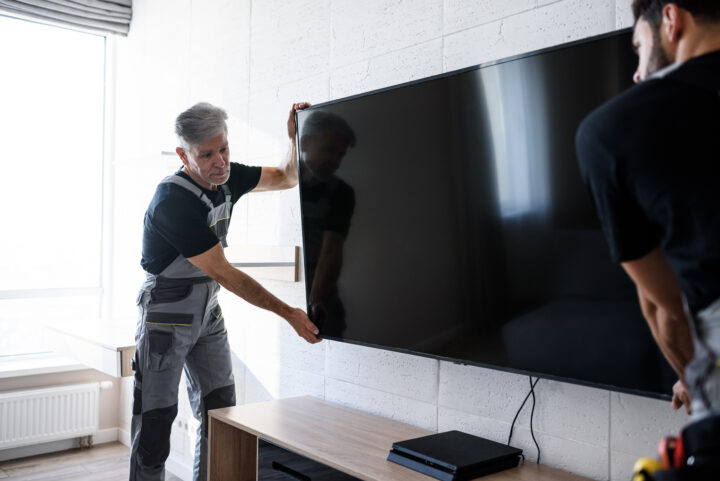 Installers mount a TV on a hotel wall