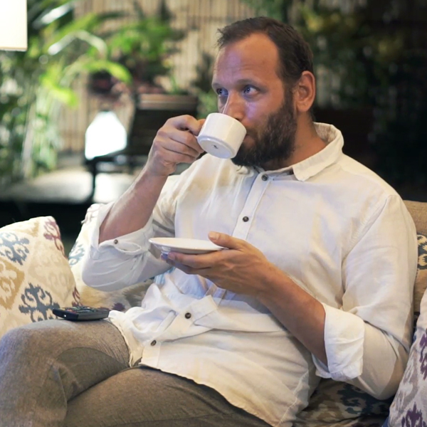 Person drinking coffee and watching TV with remote control on his lap