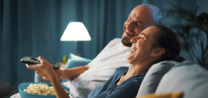 Happy couple watching television in a hotel bed