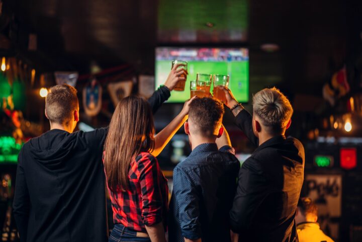 People in a restaurant are toasting and watching sports on TV