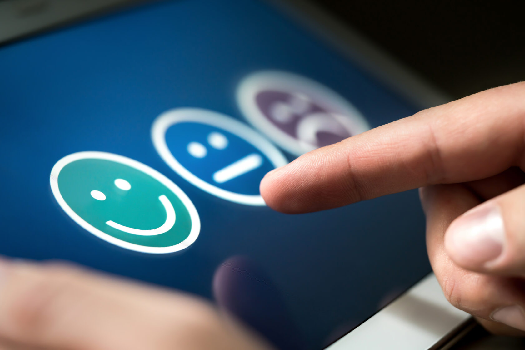 Finger points at a digital screen with three face icons for feedback: happy, neutral, and sad.